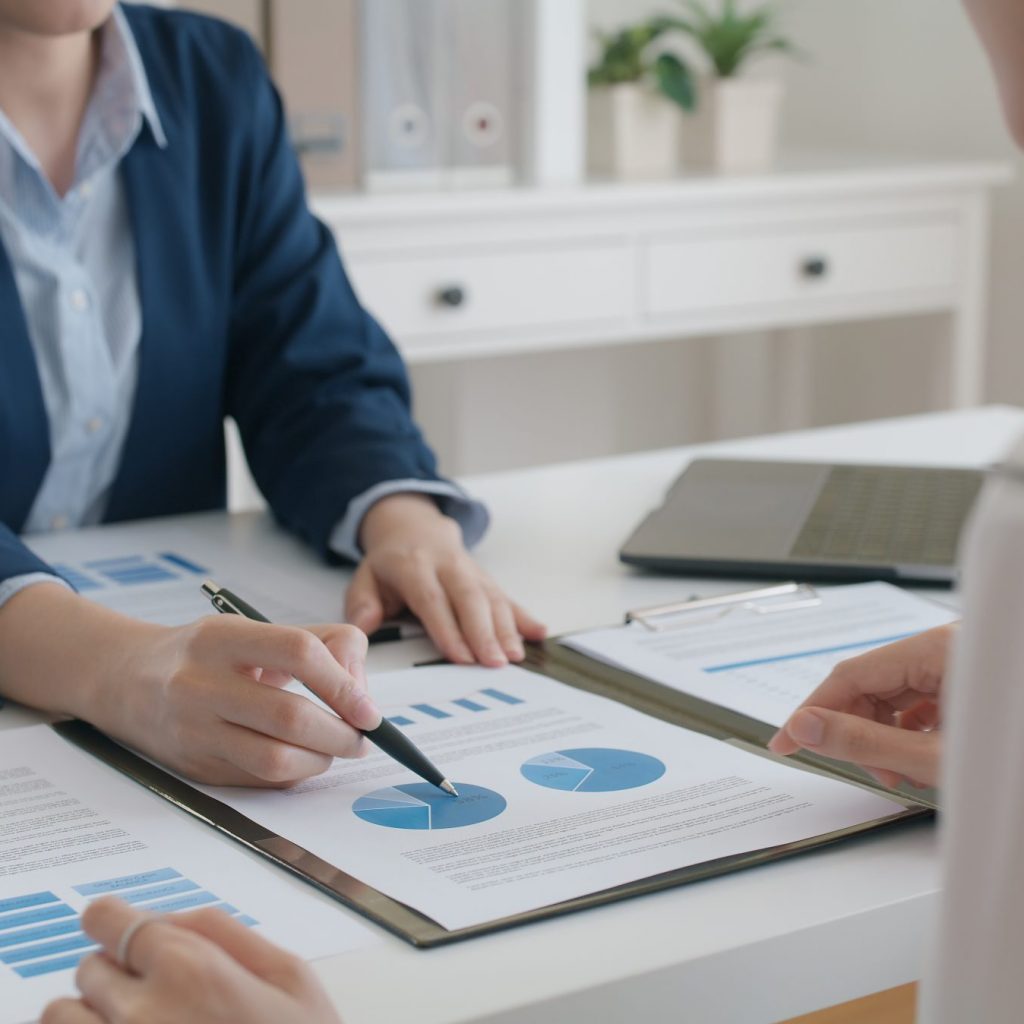 Asia stock trader agent or Sale tax loan broker advice brief and point hand to graph report talk to client at office desk show budget chart data or legal result on claim form. Trust will in work plan.